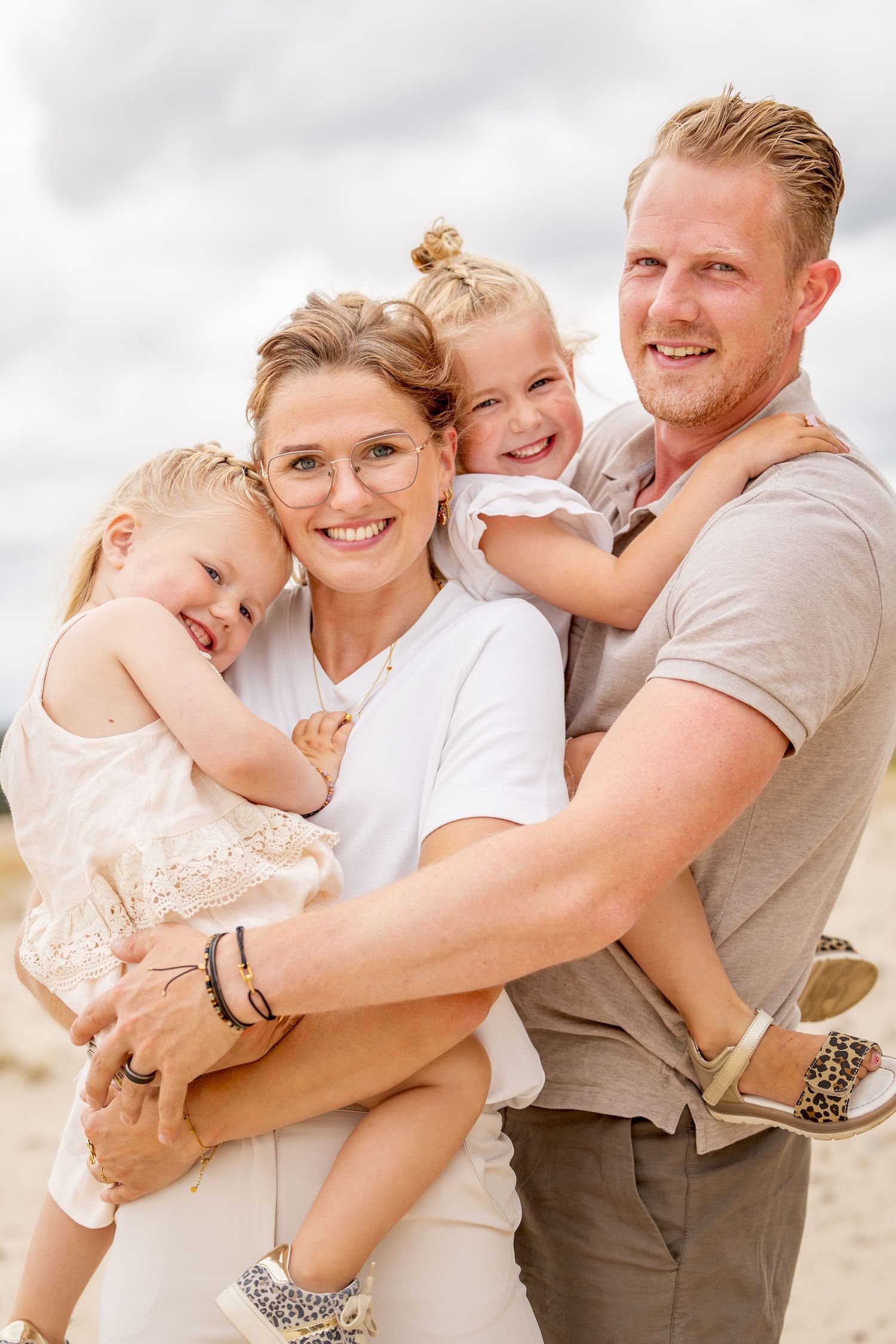 gezinsfoto waarbij papa en mama allebei een dochter optillen en dicht tegen elkaar aan staan