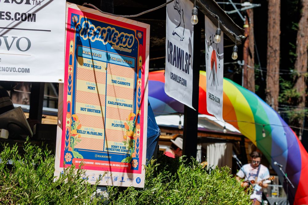 Colorful Pride event signage with rainbow flag decorations displayed outdoors at a sunny festival venue.