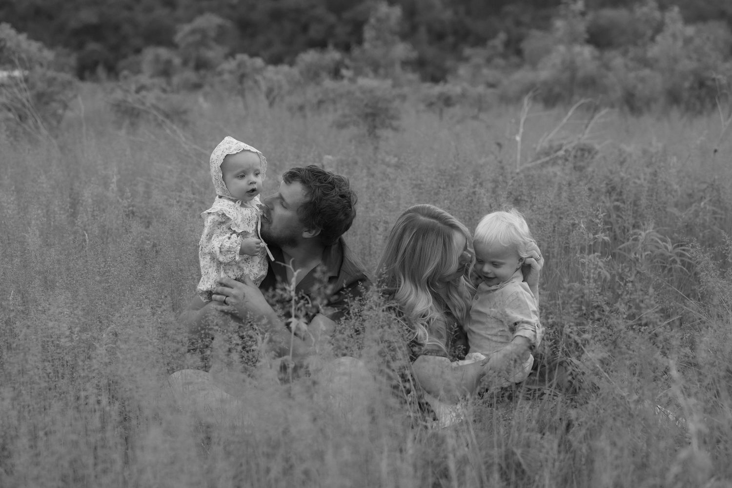 Candid family photo of parents and toddlers sitting in a grassy field during outdoor family photos in Hudson, WI.