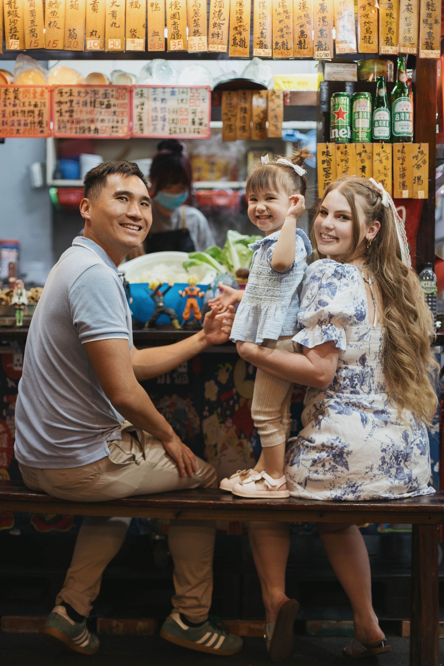 A smiling couple in white outfits sitting on vintage shop steps surrounded by plants and old utility meters.