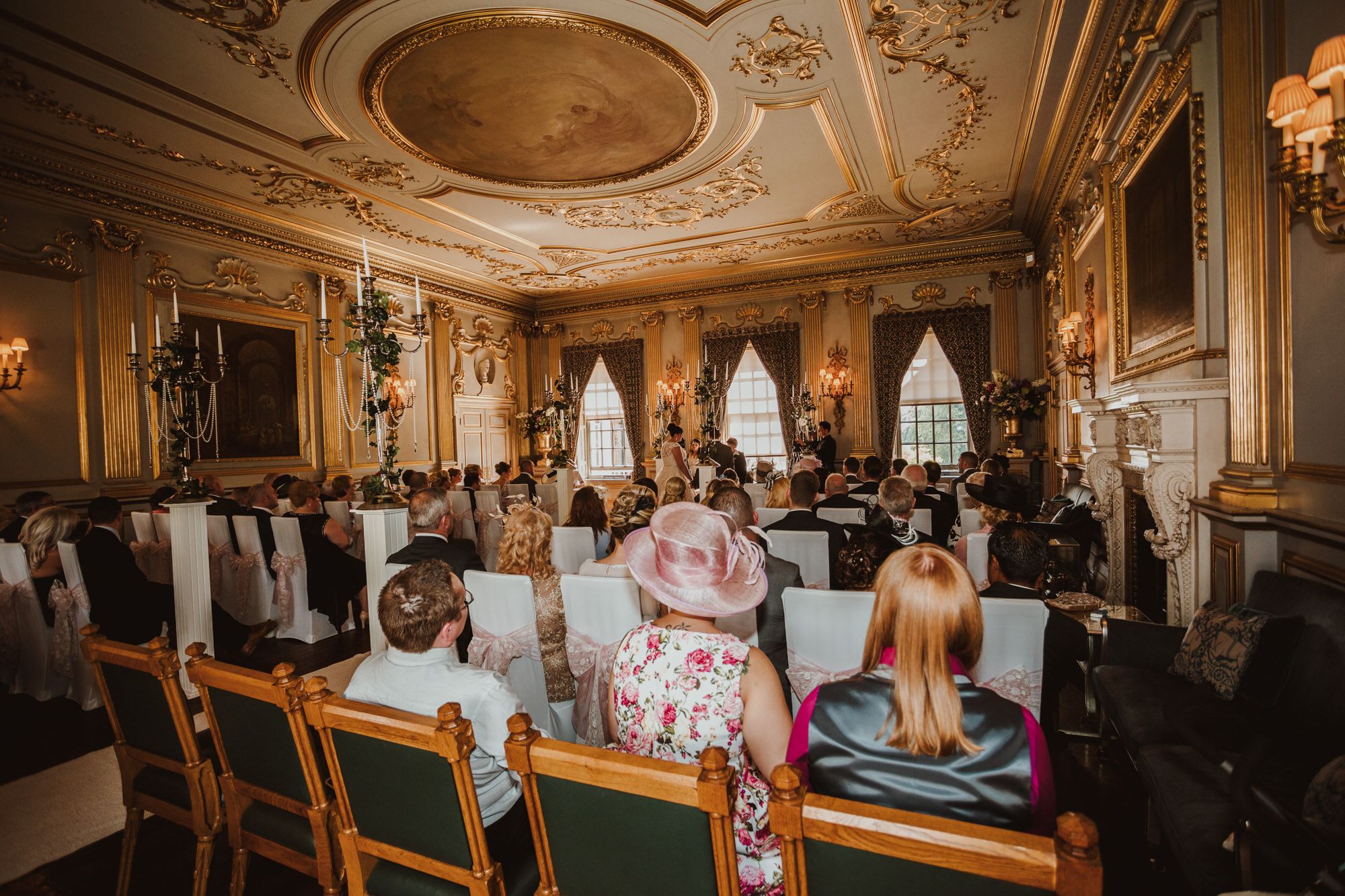 Elegant wedding ceremony in ornate golden ballroom with guests seated in rows facing the altar.