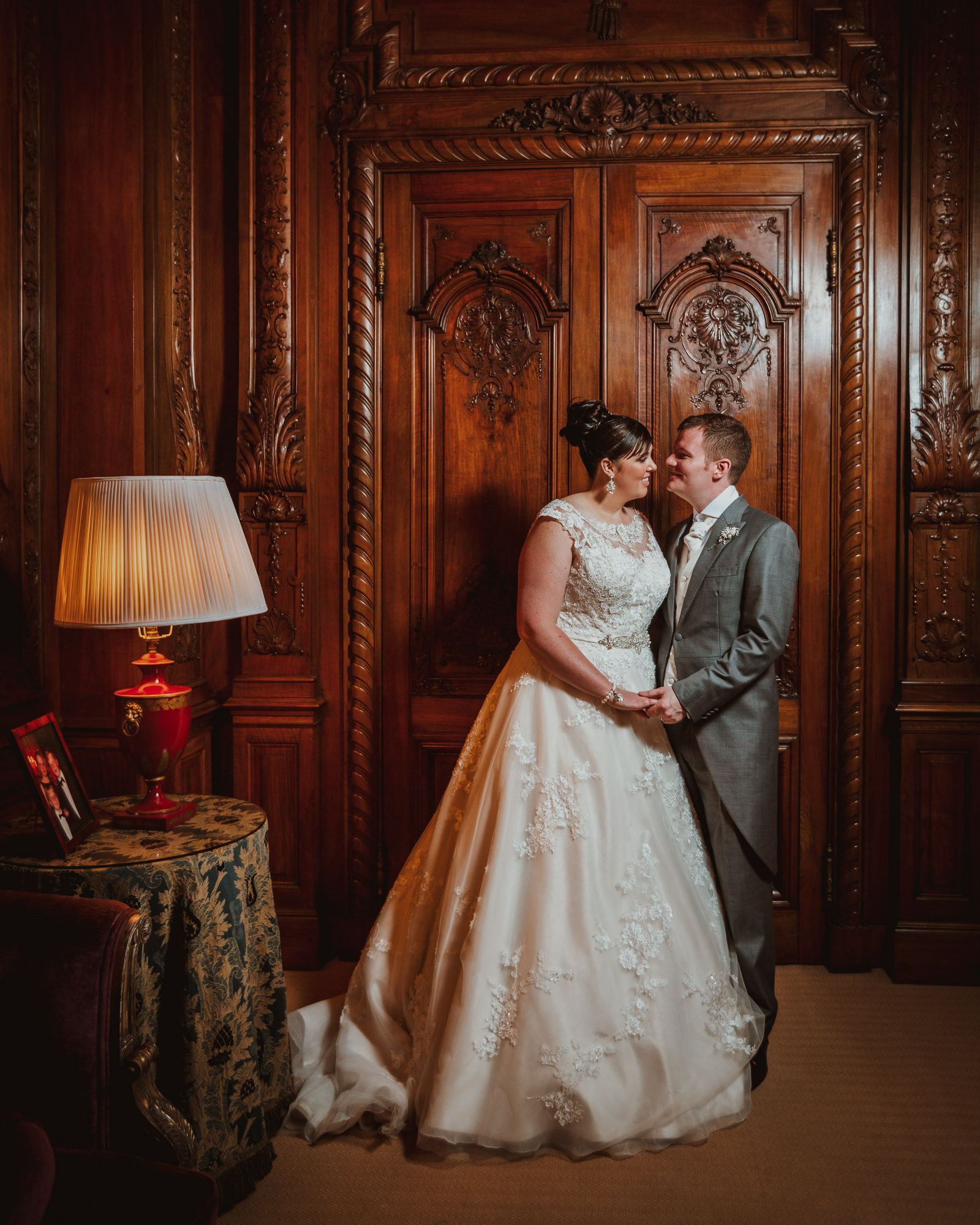 Bride and groom share a romantic moment in front of ornate carved wooden doors in an elegant wedding venue.