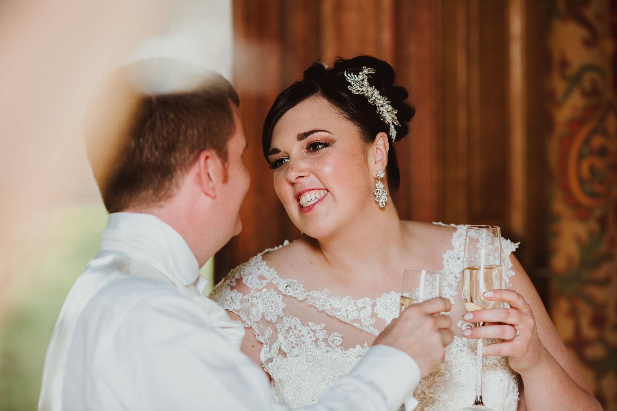 Bride and groom toasting with champagne glasses, smiling at each other during wedding reception celebration.