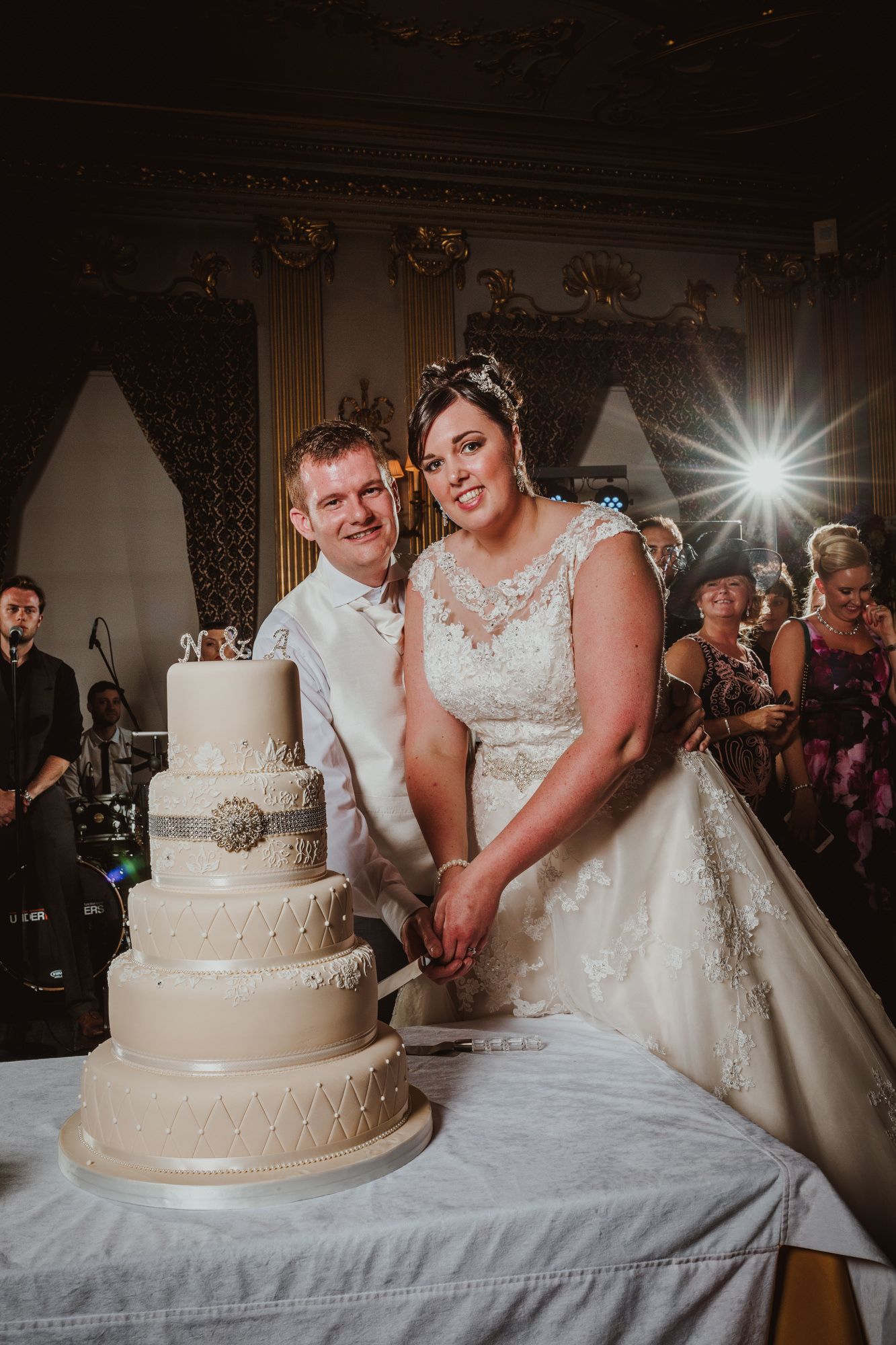 Bride and groom cutting elegant four-tier white wedding cake at formal venue reception.
