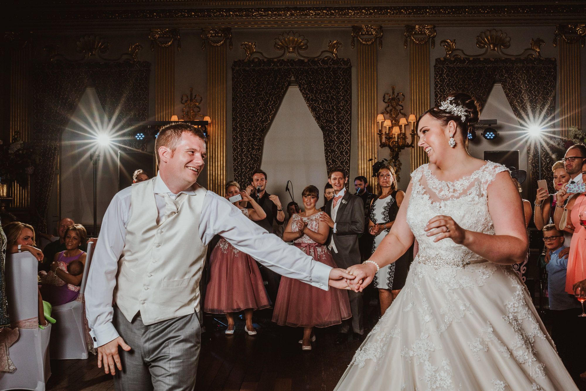 Bride and groom sharing their first dance at elegant wedding reception with guests watching in background.