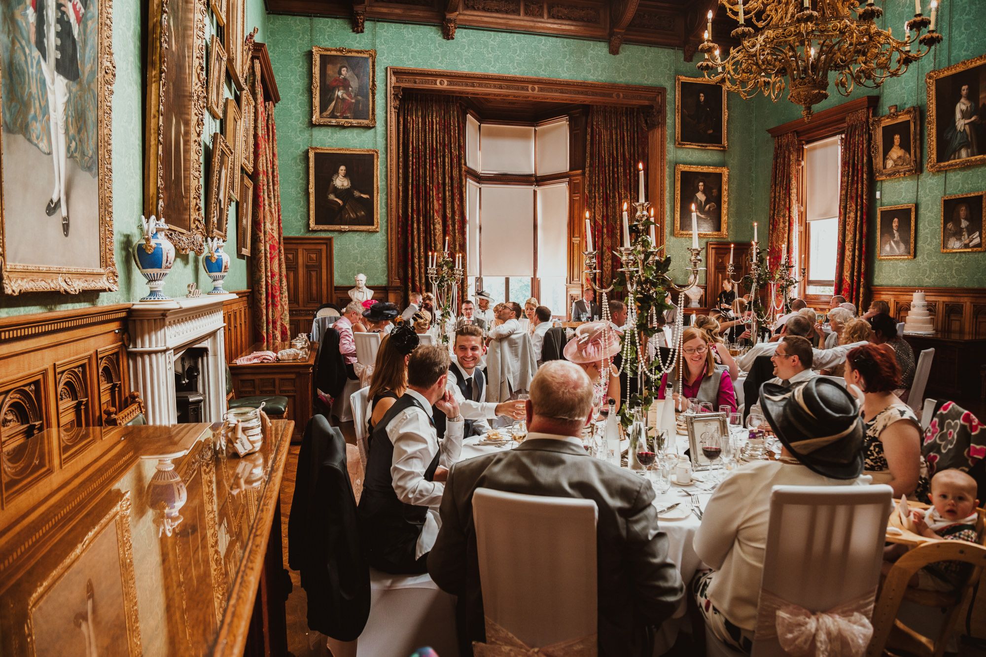 Elegant wedding reception dinner in a grand historic dining room with green walls, portraits, and candlelit tables.