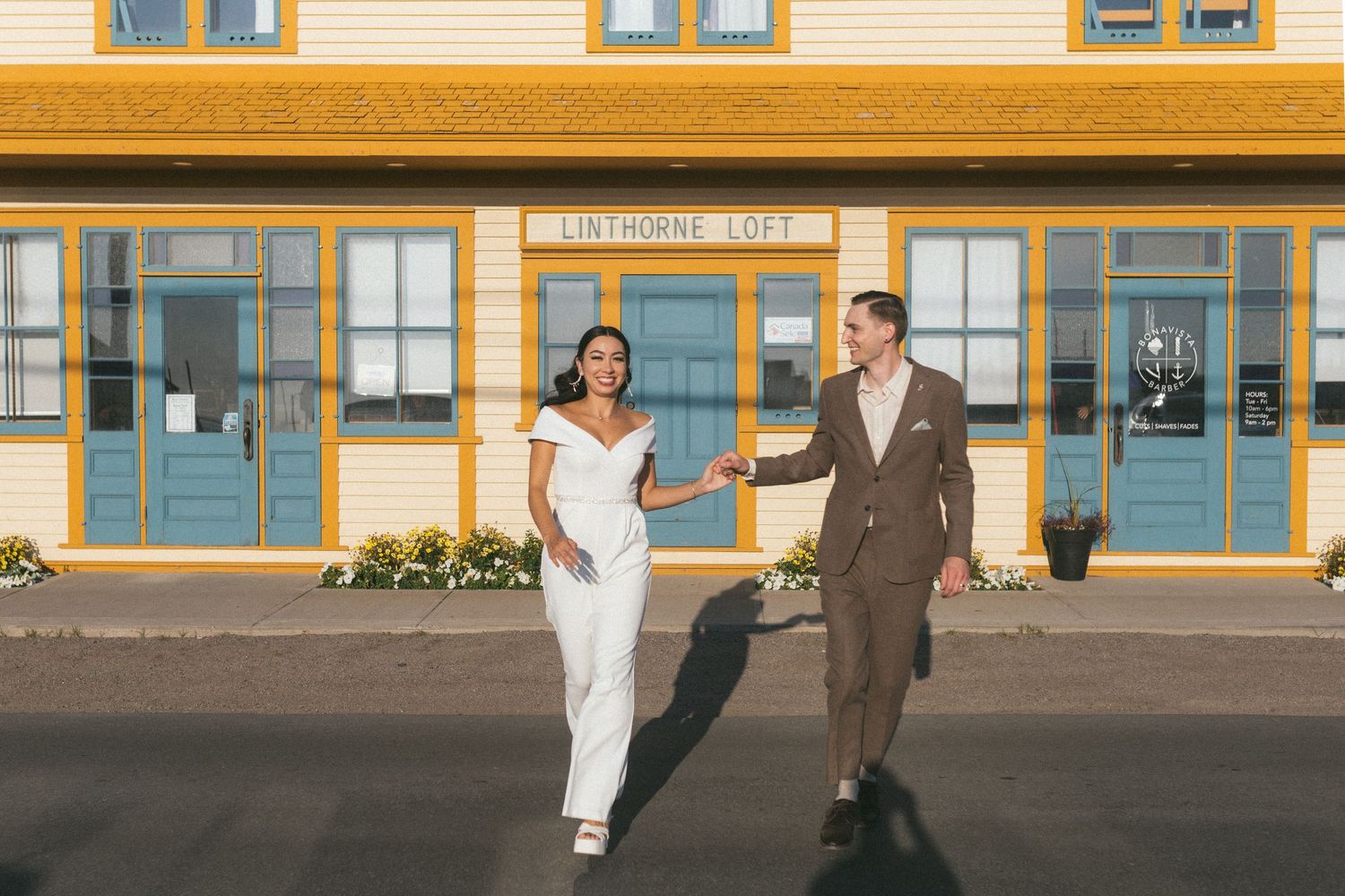 bride and groom hold hands and run across the road front of vibrant yellow and blue building