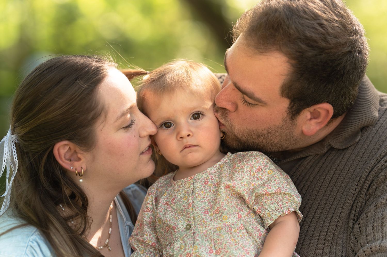 Parents qui embrassent chacun une joue de leur petite fille en robe fleurie, lors d'une séance photo famille en nature à Québec