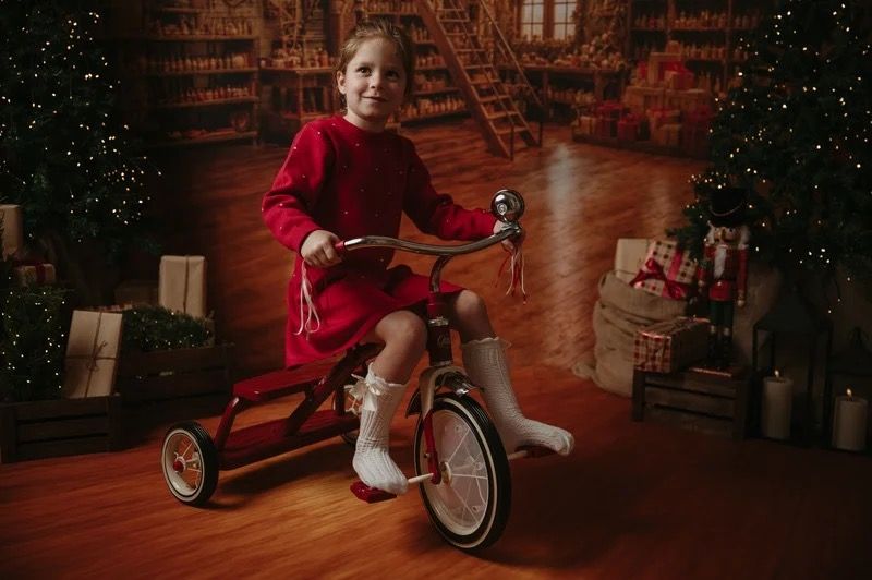 A child in red riding a red tricycle in a Christmas setting during a previous session.