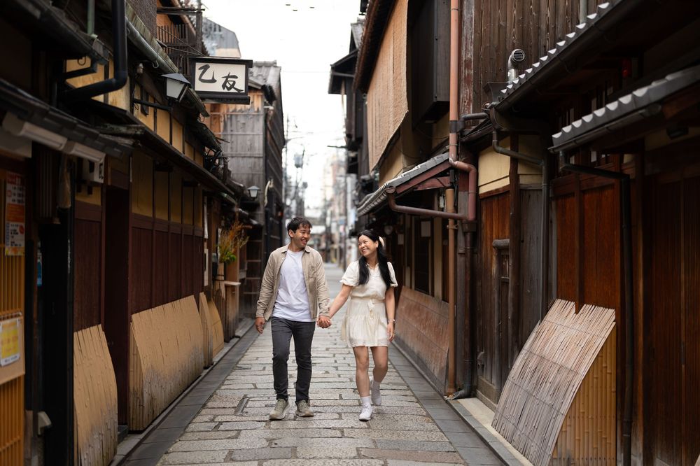 Couple holding hands and walking down a narrow cobblestone alley lined with traditional wooden buildings in a historic Japanese district.