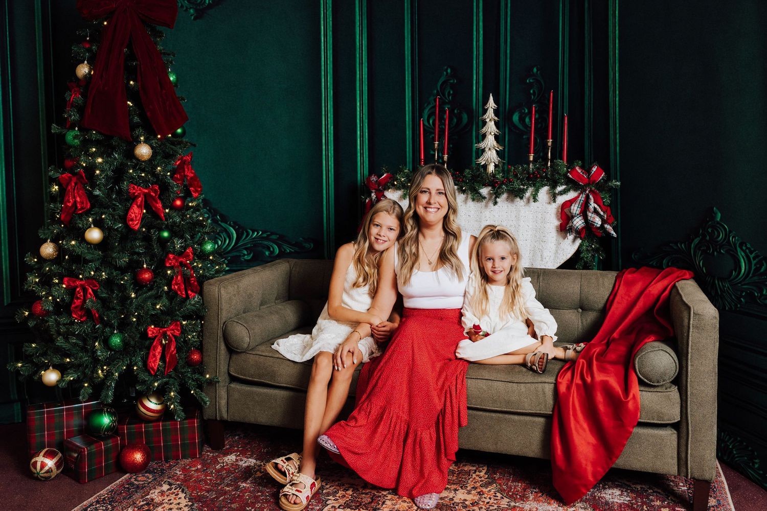 A mother and two daughters pose on a sofa with a Christmas tree for studio portraits. Christmas Mini Sessions in Middletown, PA