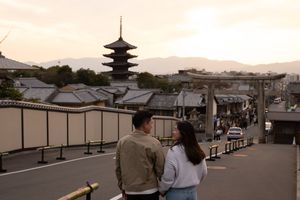 Couple standing together on a quiet street at sunset, with a historic Japanese pagoda and a stone torii gate in the background.
