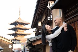 Smiling couple embracing on a traditional Kyoto street with wooden buildings and the Yasaka Pagoda rising in the background at dusk.