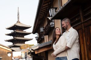 Smiling couple embracing on a traditional wooden street in Kyoto with the Yasaka Pagoda rising in the background at sunset.