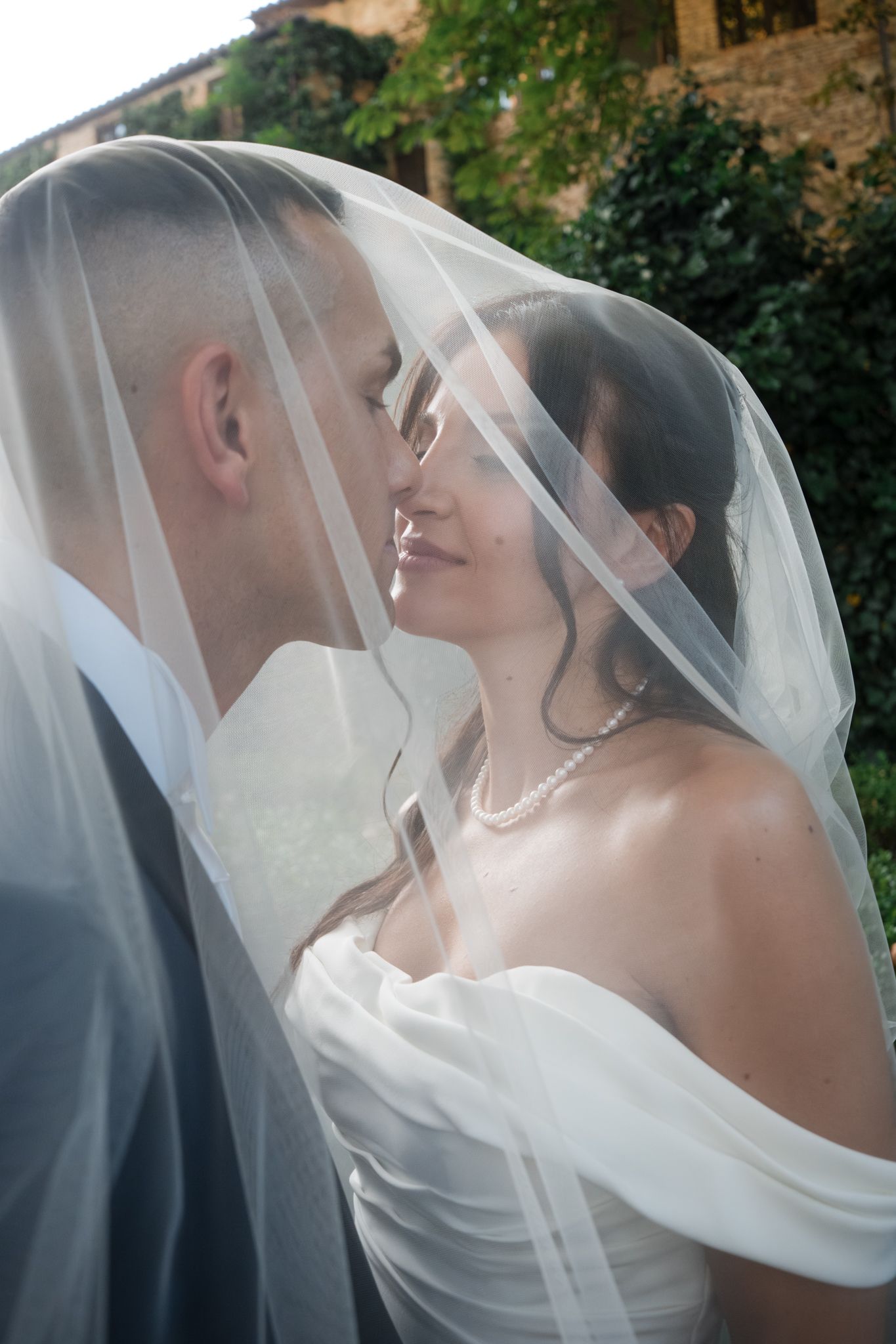 Black and white photo of a groom kissing bride on cheek outdoors with windswept hair.