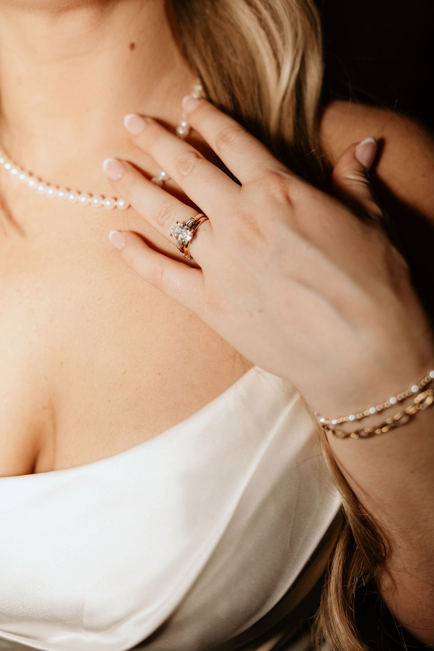 Bride wearing a diamond halo engagement ring, pearl bracelet, and pearl necklace with a white satin wedding dress.