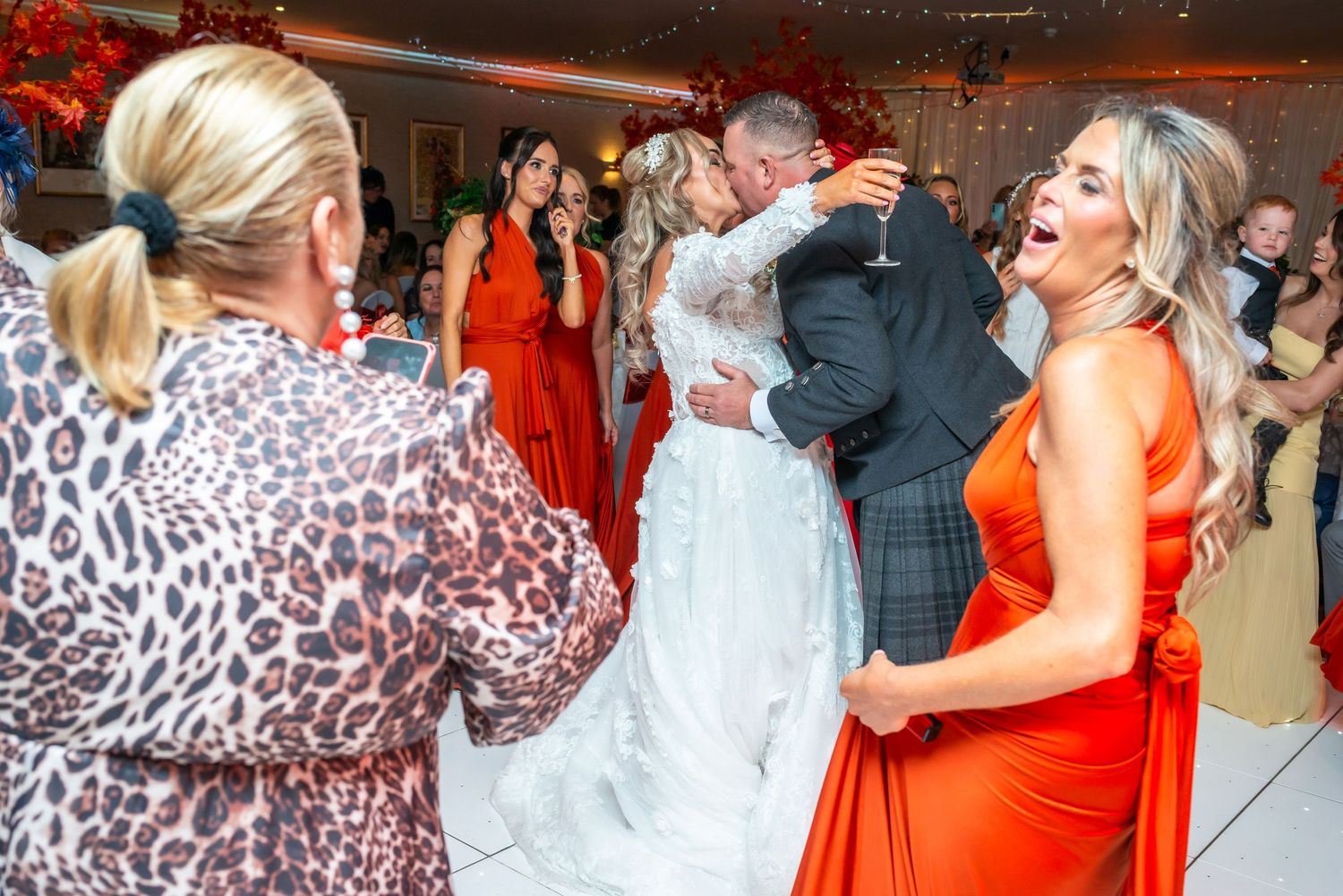 Bride and groom share a kiss on the dance floor surrounded by joyful guests in elegant attire at a wedding reception at Parklands, Widnes