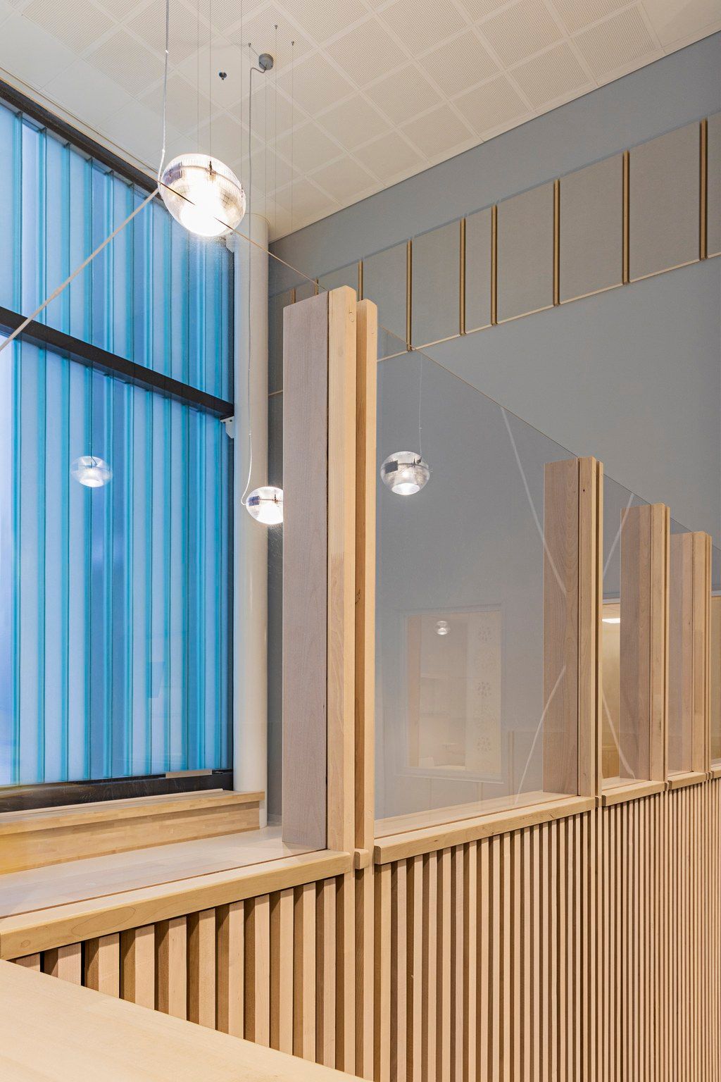 Modern interior with wood slat panels, glass partitions, pendant globe lights, and a blue striped window in a contemporary space.