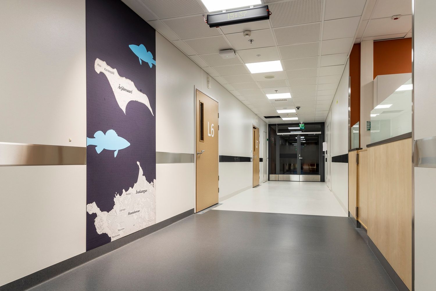 Modern hospital corridor with colorful wall mural, wooden doors, and clean flooring in a healthcare facility.