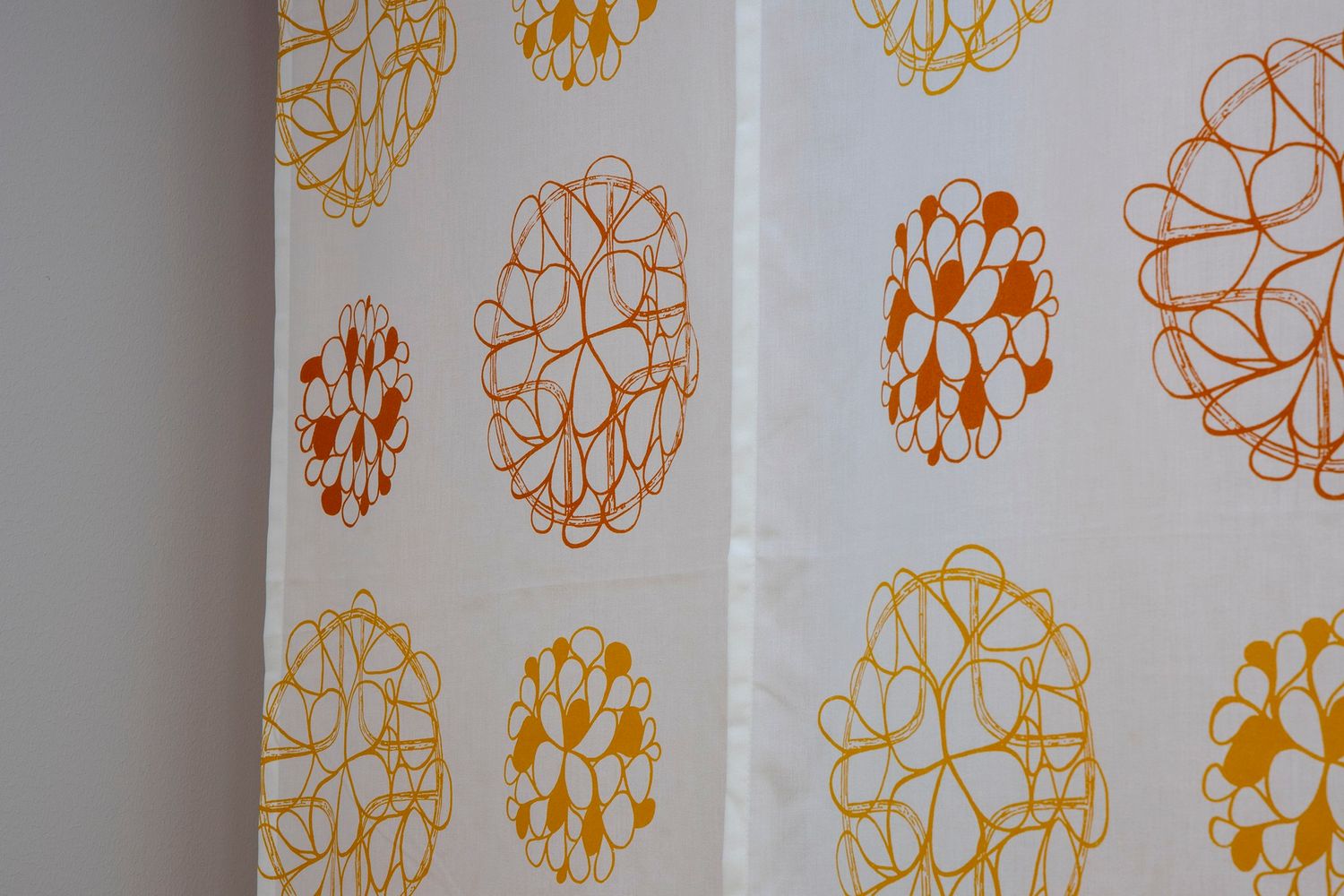 White fabric with orange and yellow floral circle patterns in a retro mid-century modern design style.