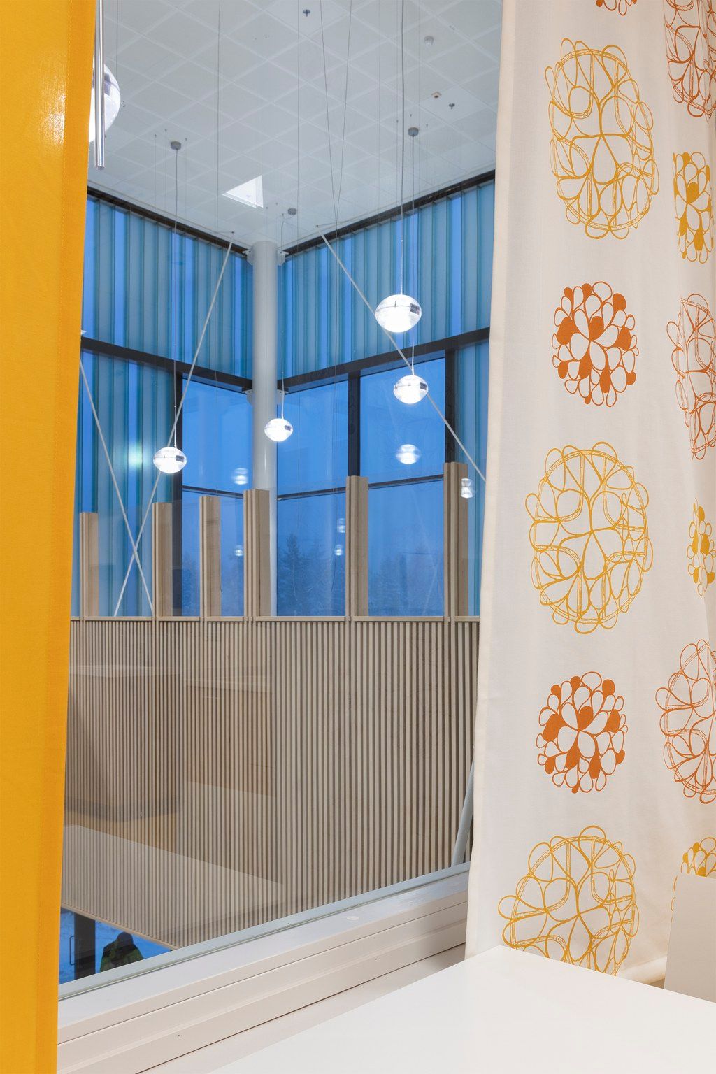 Modern interior with floral curtain, pendant lights, blue windows, and wooden slat partition in a contemporary space.