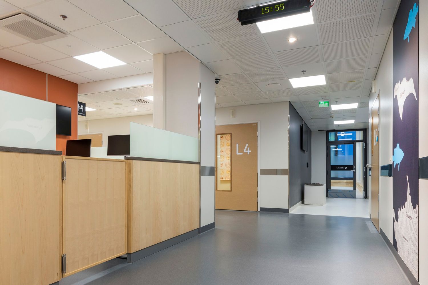 Modern hospital corridor with L4 ward signage, wooden reception desk, colorful wall murals, and bright fluorescent lighting.