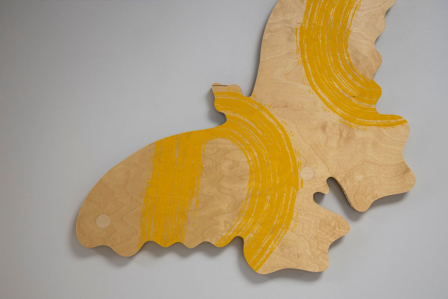 Yellow and beige butterfly-shaped paper mache wall art sculpture with curved stripe details on gray background.