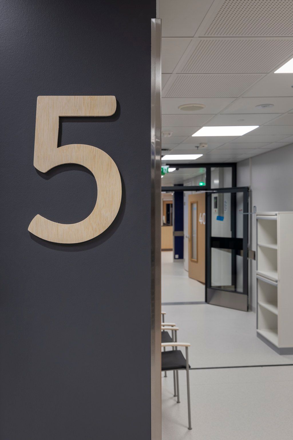 Modern hospital corridor with a large wooden number 5 sign on a dark gray wall, leading to a bright hallway.