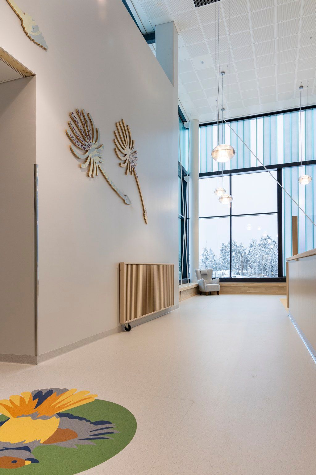 Bright modern hospital hallway with decorative dandelion wall art, colorful floor rug, and large windows with snowy view.
