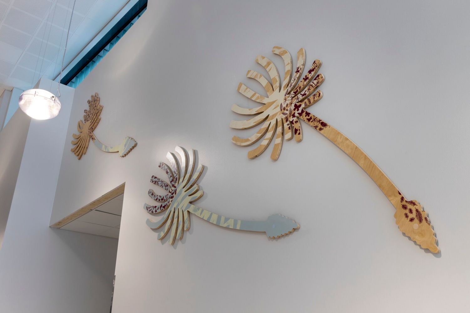 Abstract botanical wall sculptures in gold and sage green mounted on a white gallery wall with pendant lighting.