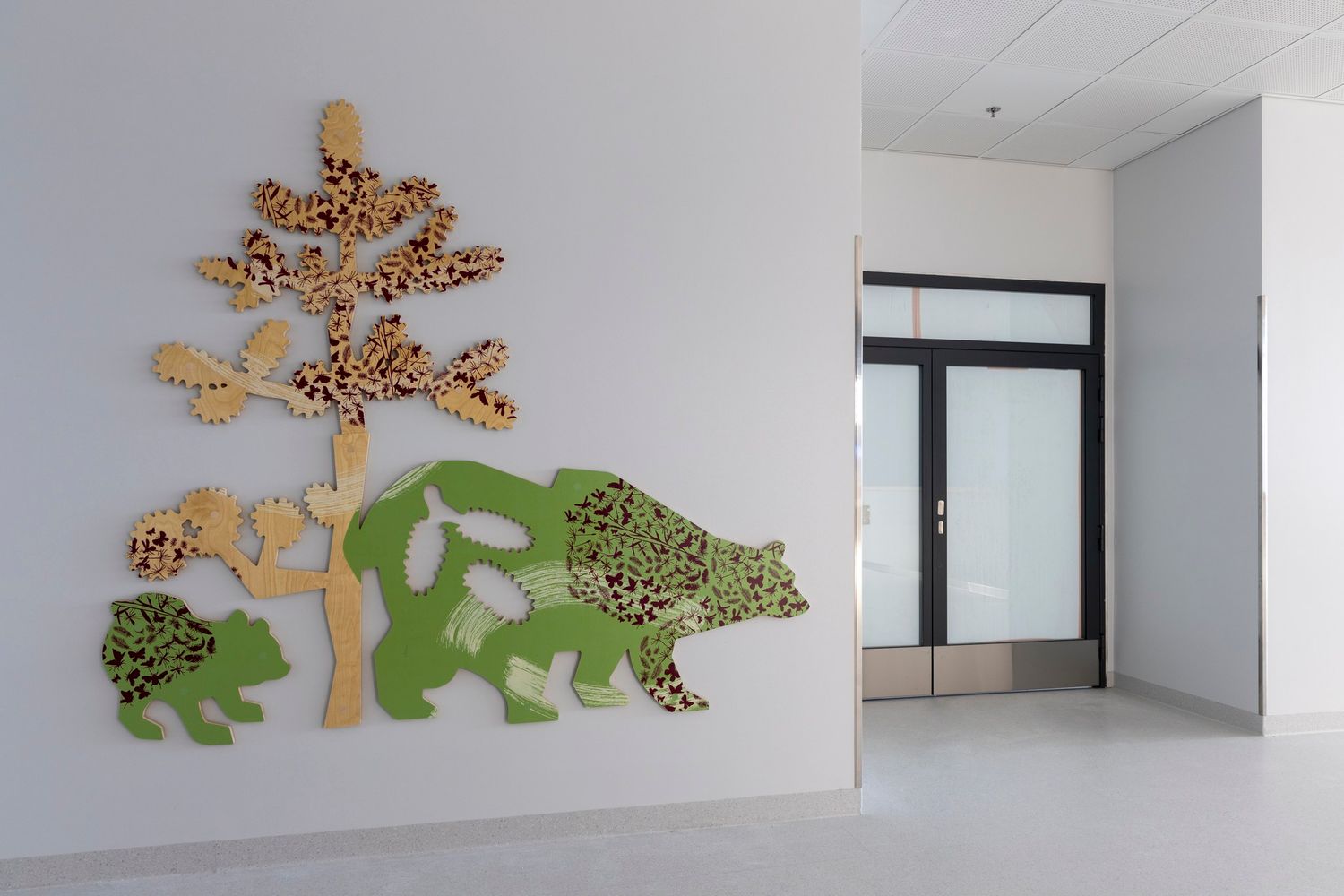 Colorful wooden bear and tree wall art decoration in a modern children's facility hallway.
