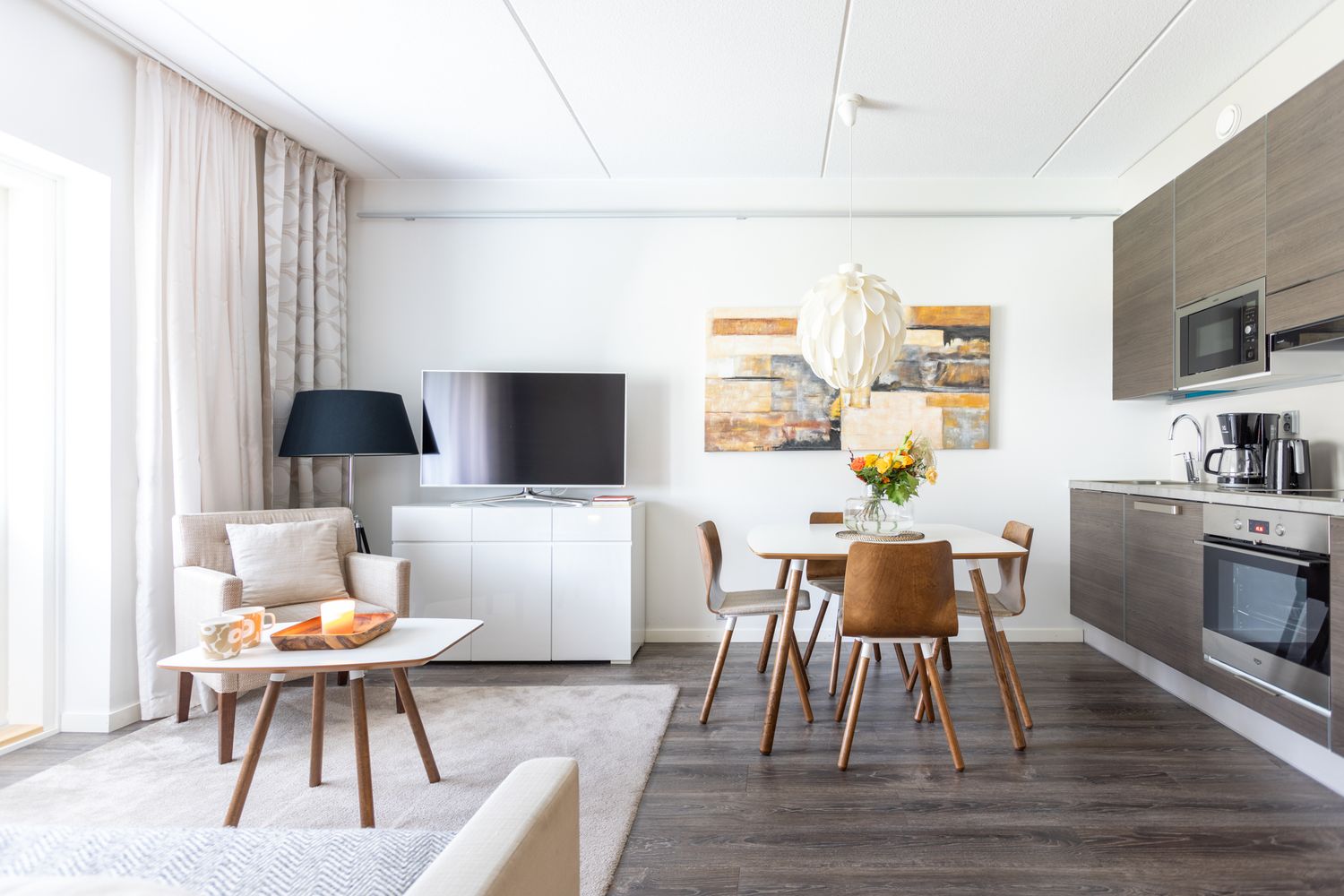 Modern open-plan apartment with dining area, kitchenette, and living space featuring neutral tones and wooden accents.