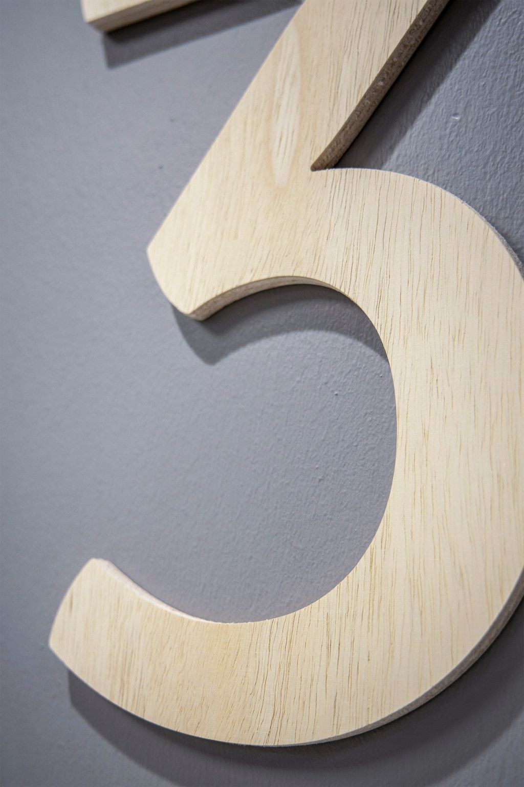 Close-up of a wooden number three mounted on a gray wall, showcasing natural wood grain texture.