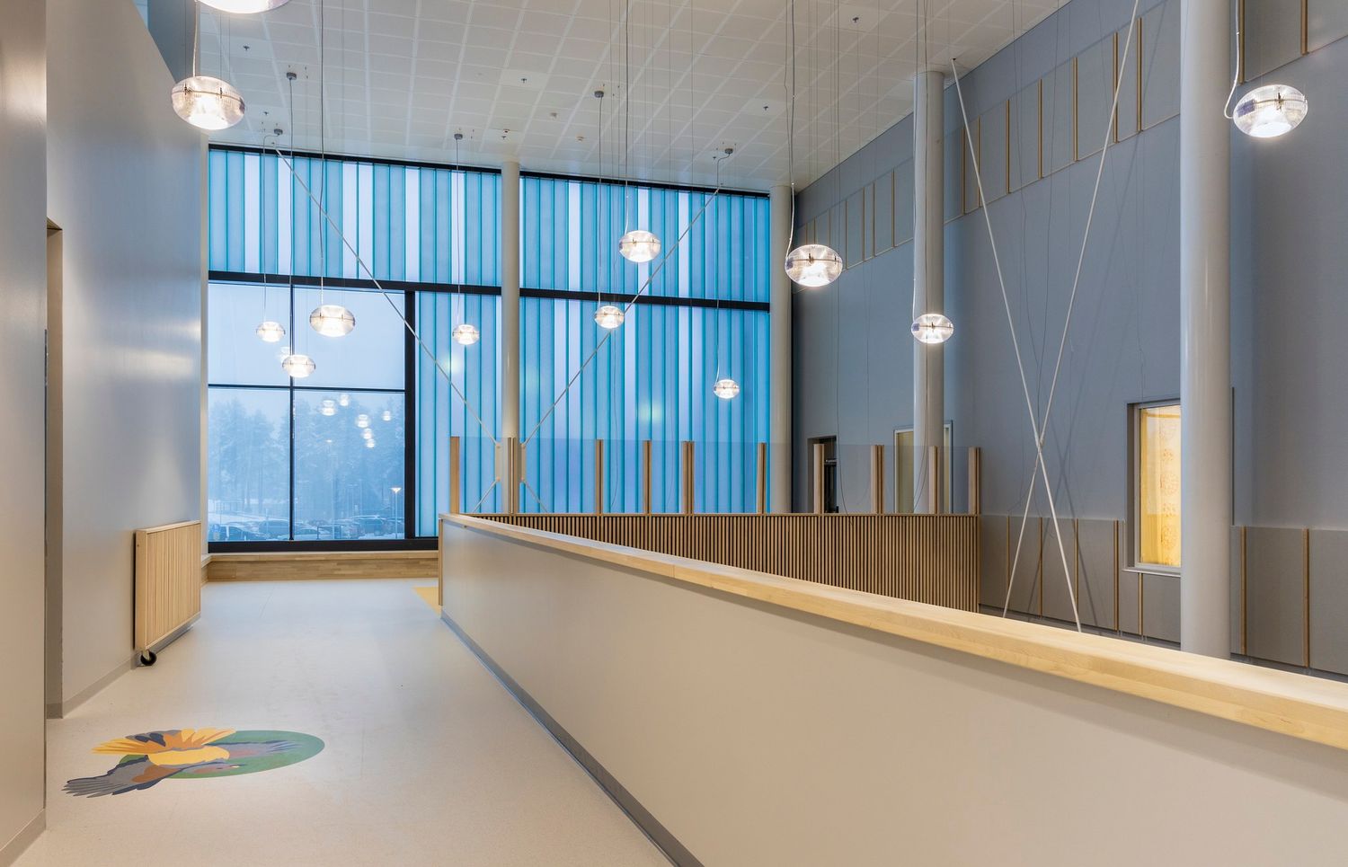 Modern pediatric facility reception area with blue accents, pendant lights, and colorful floor art.