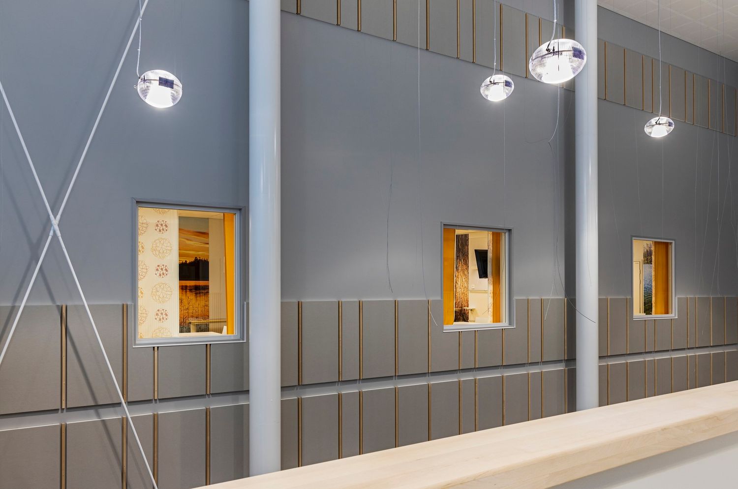 Modern interior hallway with gray walls, wooden accents, square windows, and elegant pendant lights.