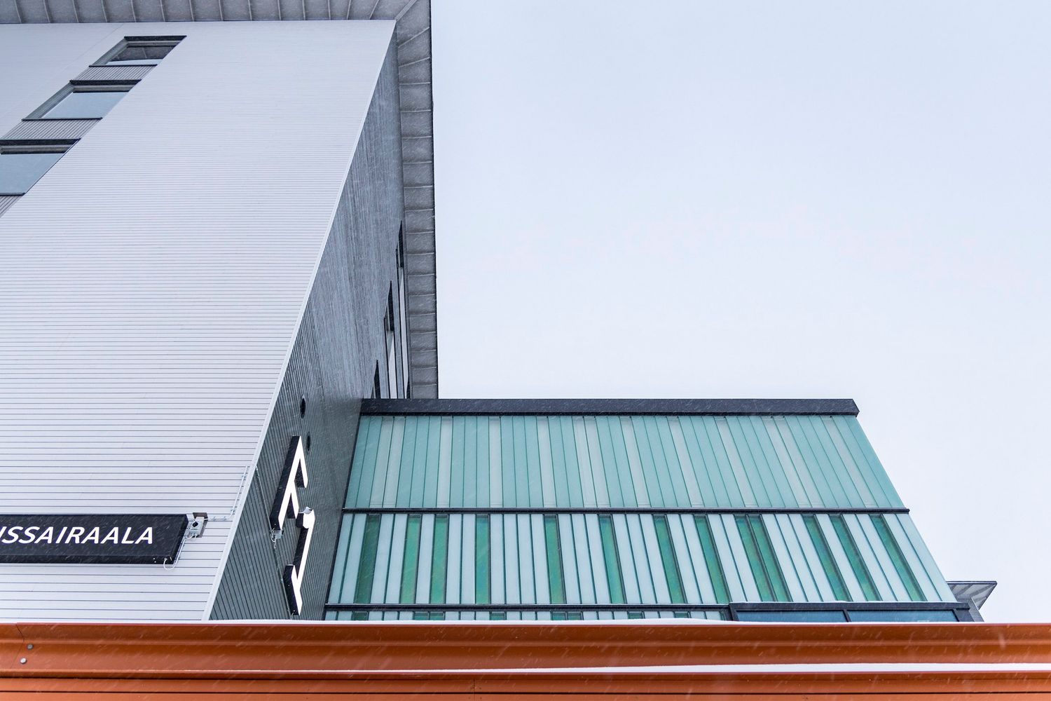 Modern hospital building exterior with green and white striped glass facade against overcast sky.
