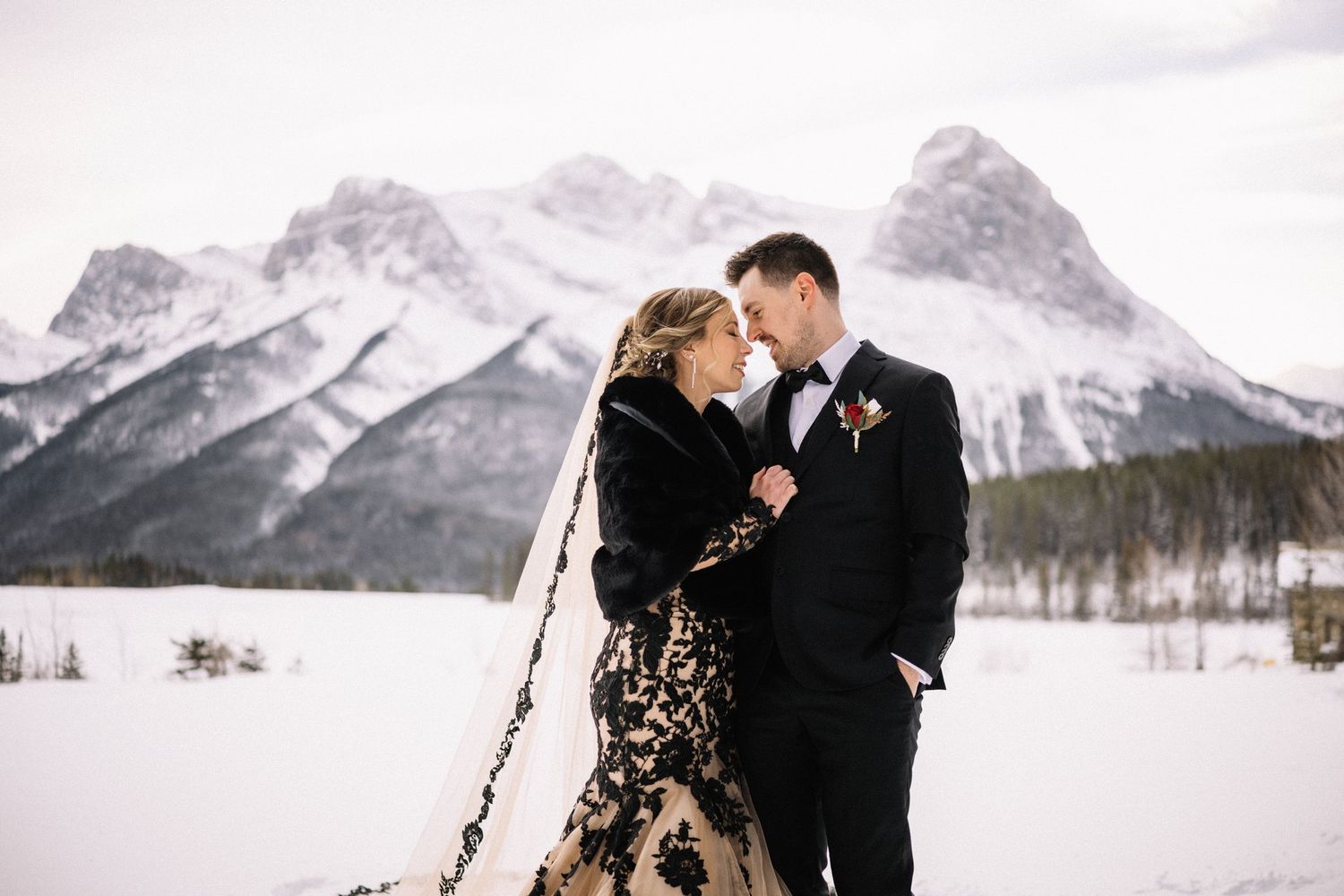 Couple touching foreheads in a snowy field in front of jagged snow-covered peaks near Canmore