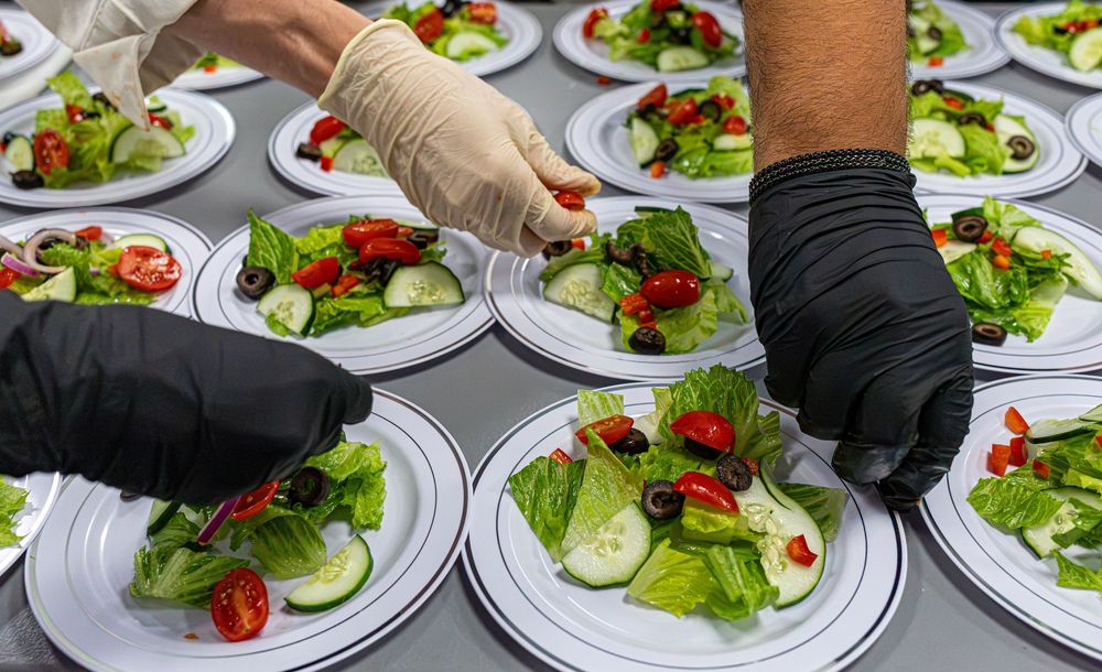 Culinary students in gloves arrange fresh garden salads on white plates for service.
