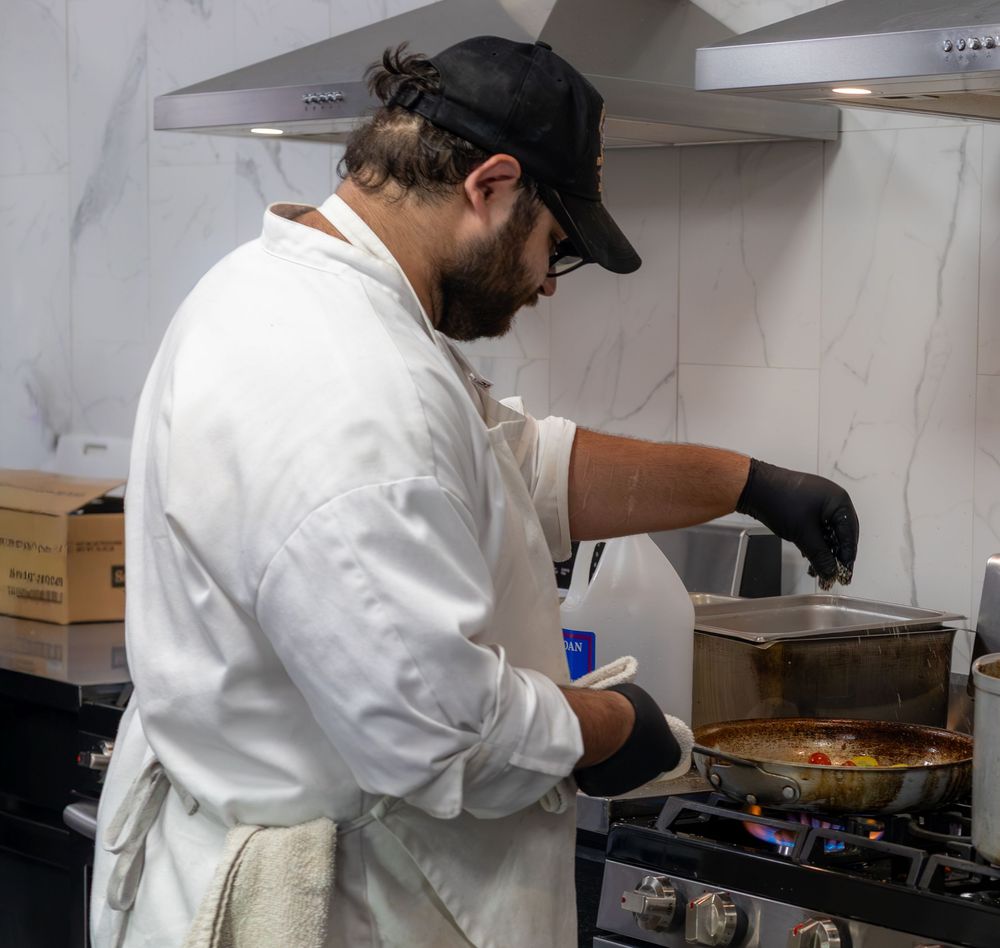 Professional chef in white coat sauteing colorful vegetables in pan over gas stove.