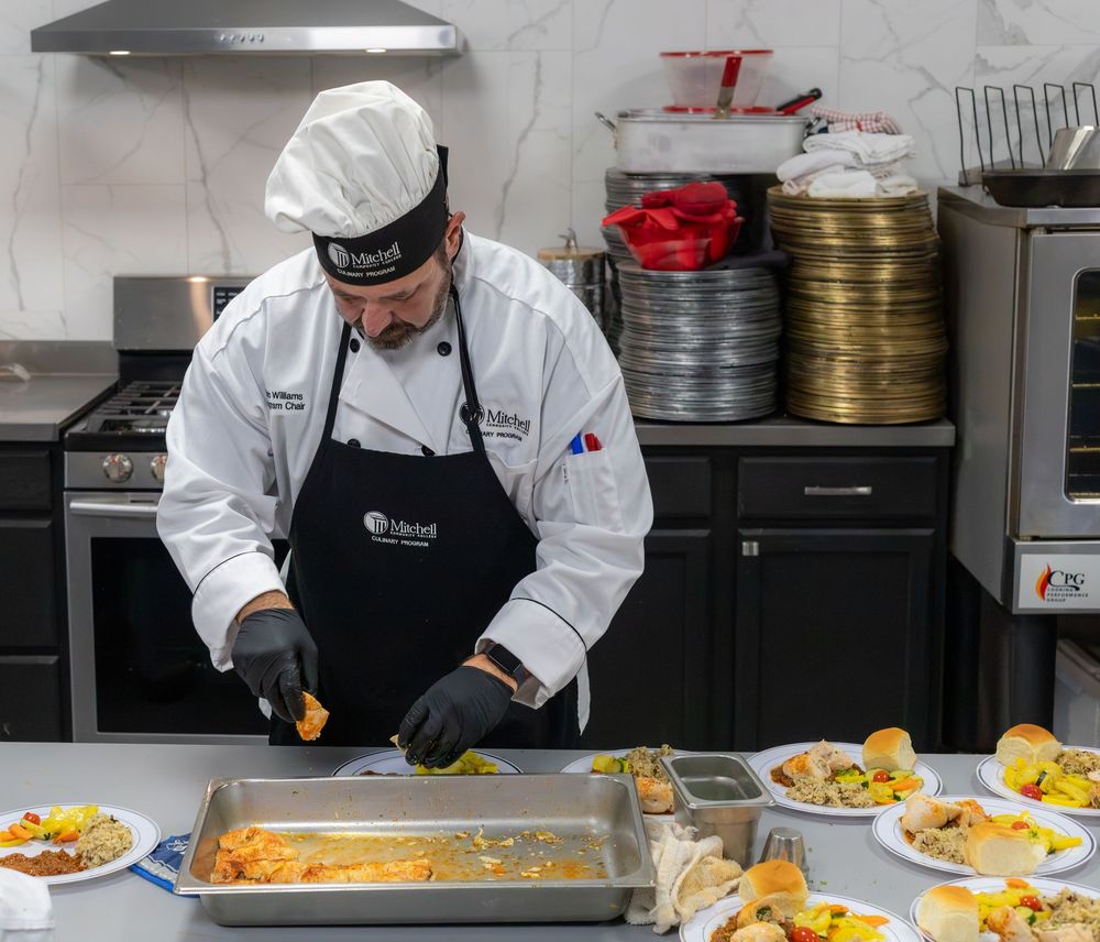 A chef in white uniform plates multiple gourmet dishes in a professional kitchen.