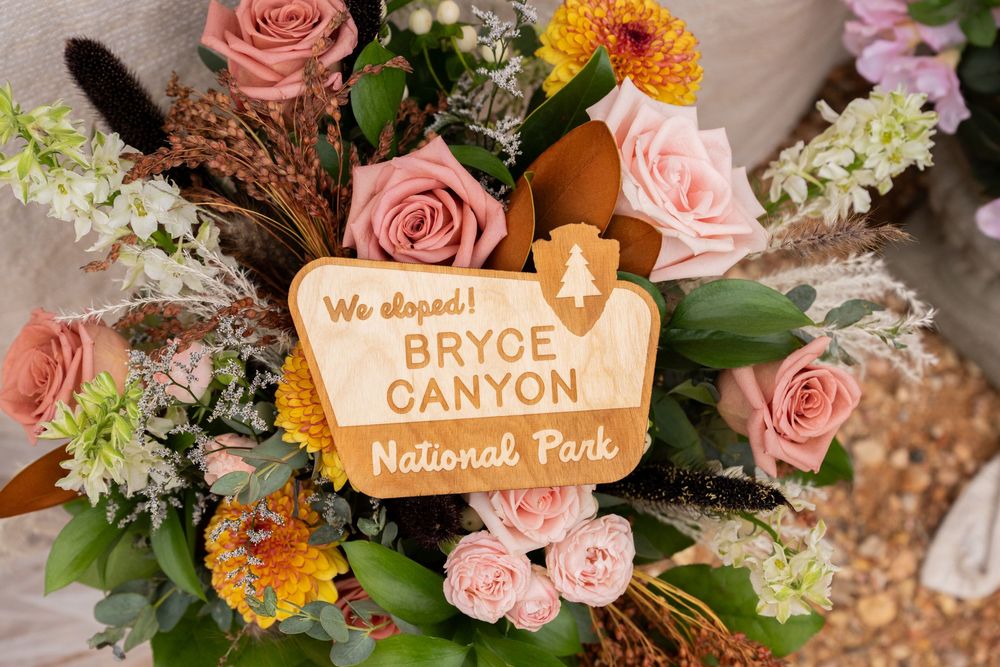 Bryce Canyon National Park elopement sign surrounded by pink roses and colorful wildflowers in a rustic floral arrangement.