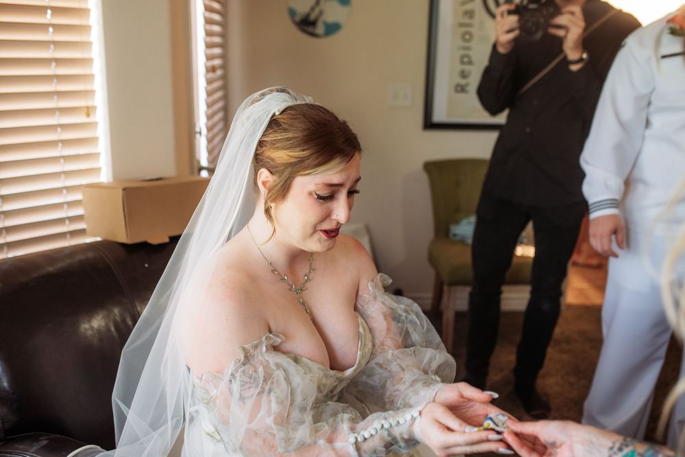Bride in floral gown and veil examining wedding ring while getting ready indoors.