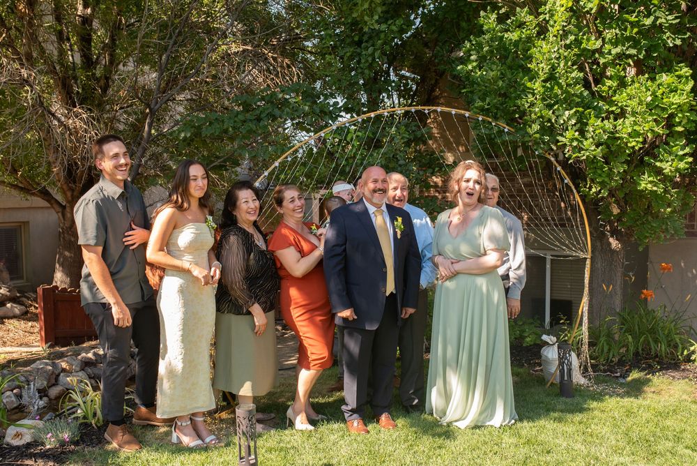 Wedding party celebrating outdoors in a backyard garden, guests in formal attire smiling during a joyful reception.