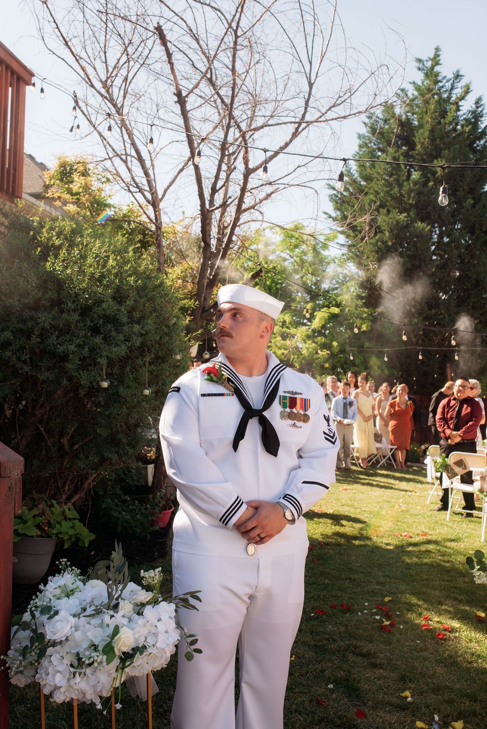 US Navy sailor in dress whites with medals standing at outdoor backyard wedding ceremony altar.