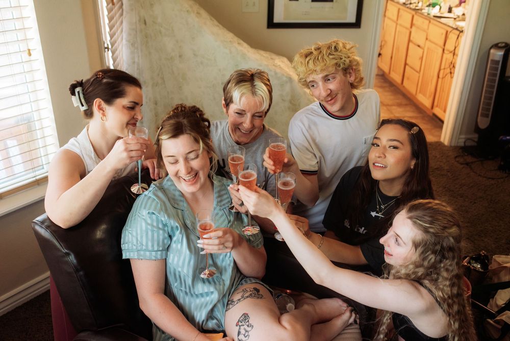 Six friends joyfully toasting with champagne glasses in a cozy room, celebrating together with big smiles.