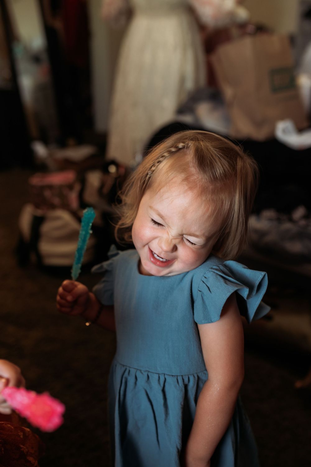 Joyful toddler girl in blue dress laughing and holding a colorful toy at a wedding celebration.