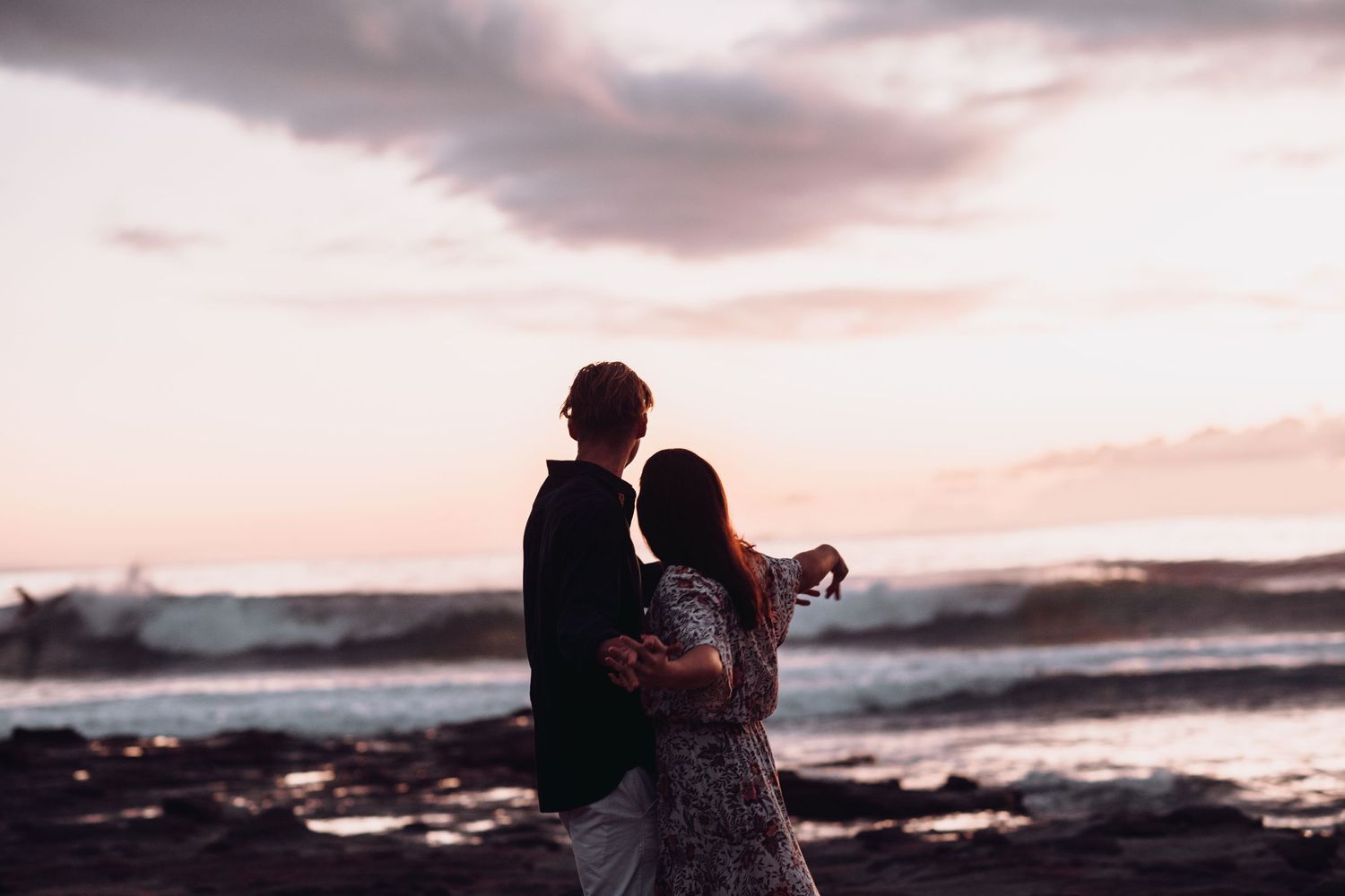 Silhouetted couple embracing on rocky beach at sunset.