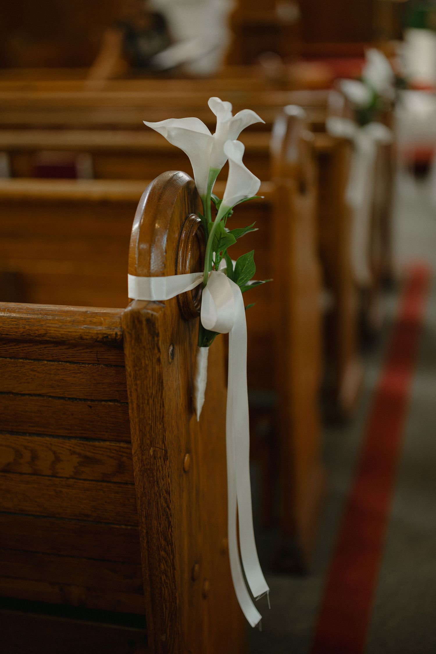 White calla lily and ribbon decoration tied to a wooden church pew along the aisle for a wedding ceremony.