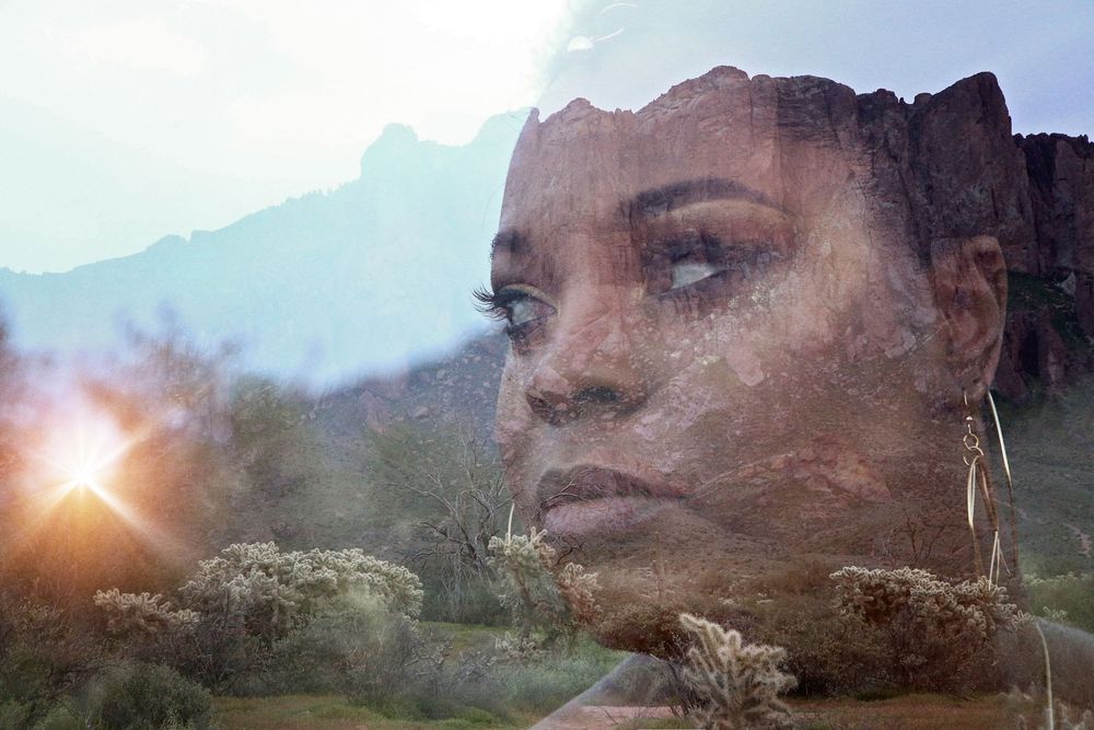 A double-exposure portrait of a woman's face blended with a desert mountain landscape and a glowing sun.