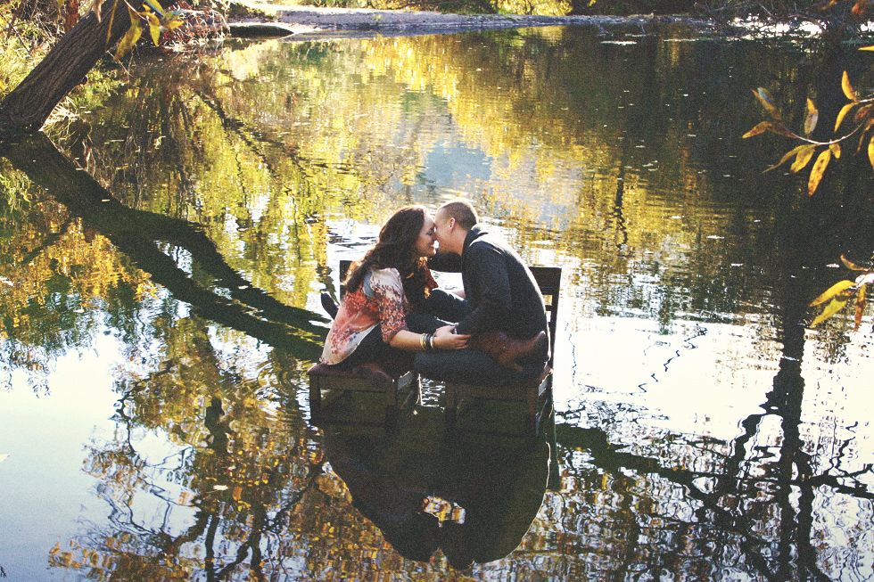 Couple kissing in a small boat on a calm lake reflecting golden autumn trees.